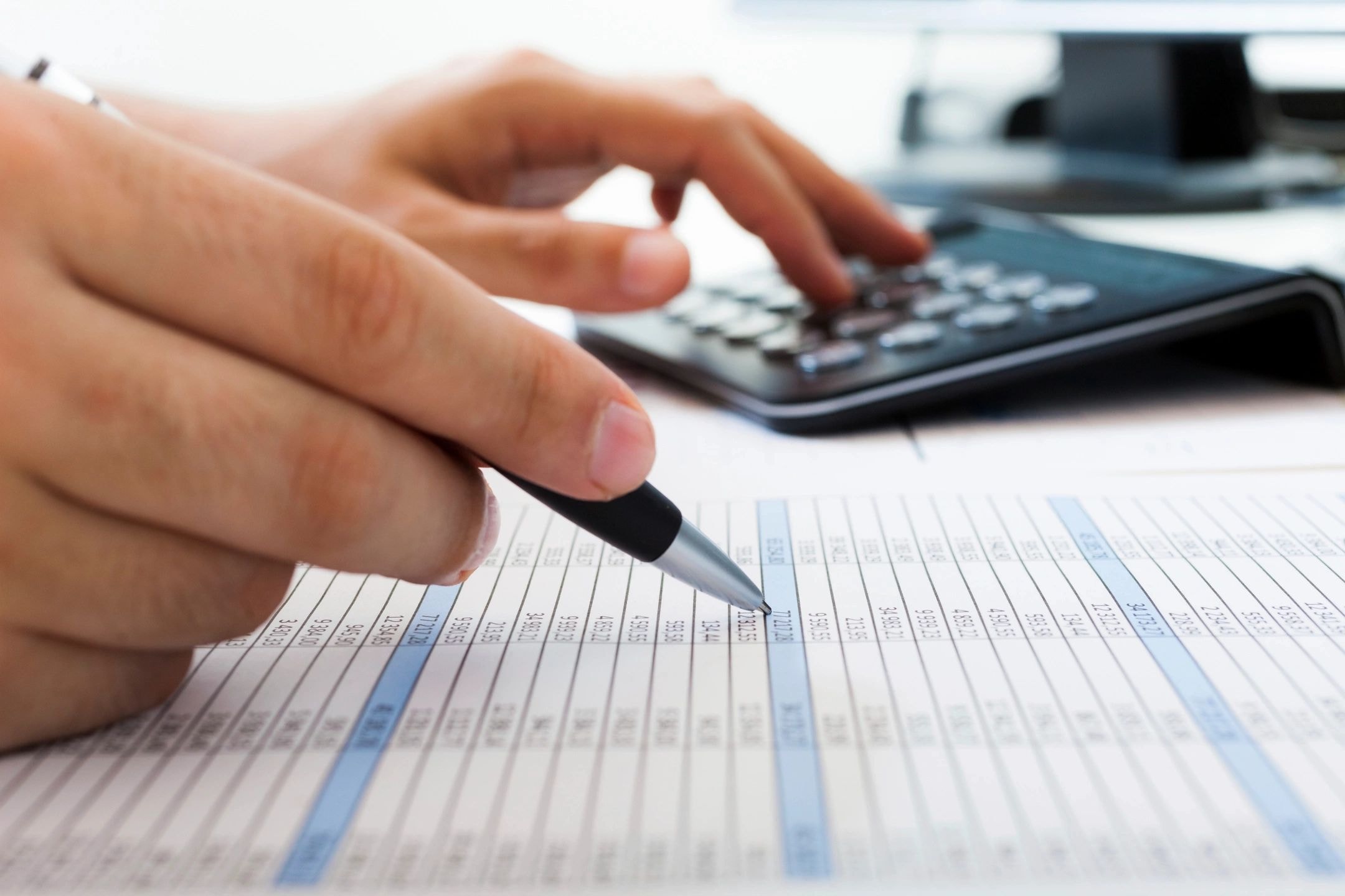 Hand holding pen pointing at spreadsheet financial document